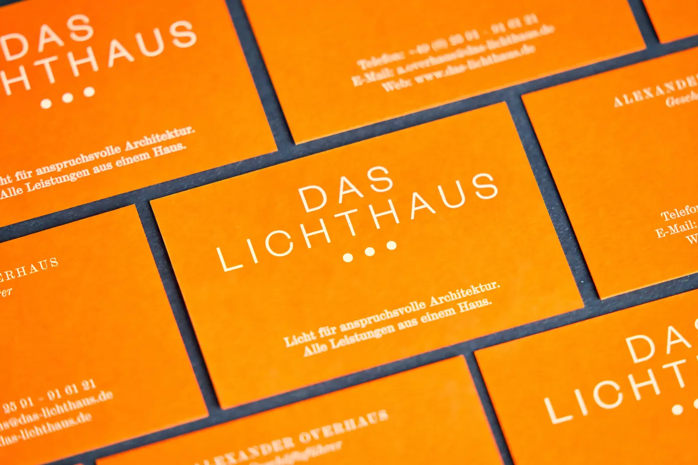 Orange Visitenkarten „Das Lichthaus“ mit weißer Schrift, versetzt auf dunklem Grund ausgelegt.