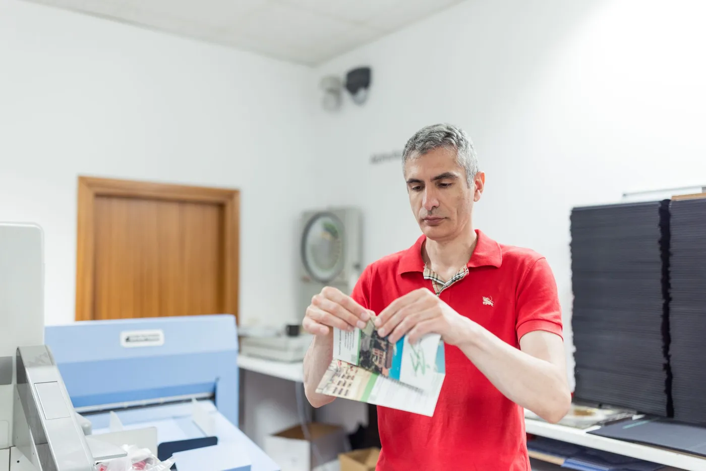 Ein Mitarbeiter im roten Poloshirt klappt einen gefalzten Flyer auseinander.