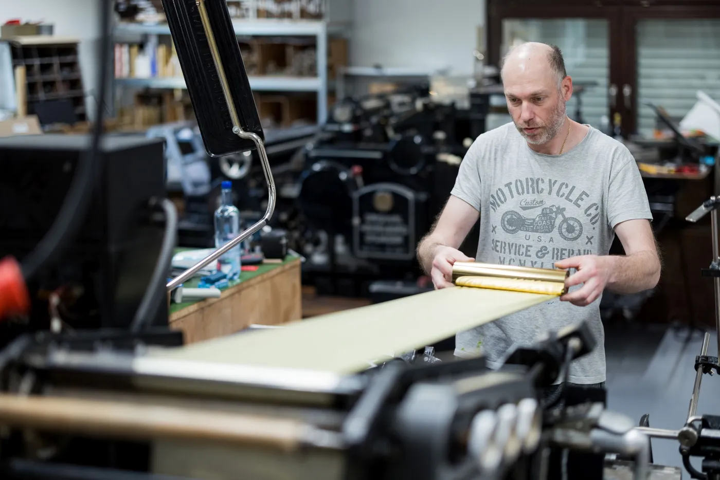 Ein Mitarbeiter führt eine Rolle Goldfolie in die Prägemaschine ein, im Hintergrund stehen weitere Tiegel.