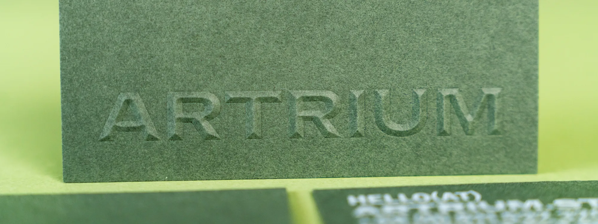 Der Schriftzug „ARTRIUM“ ist plastisch in eine olivgrüne Visitenkarte geprägt, davor unscharf weitere Karten.