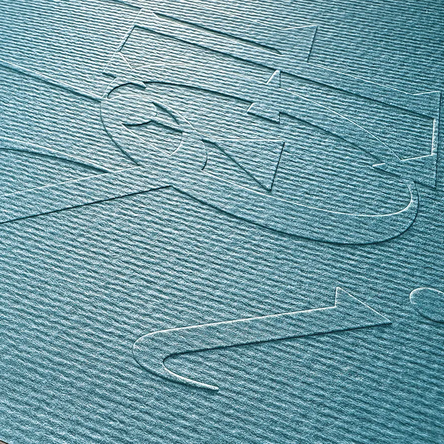 Nahaufnahme geprägter Buchstabenformen auf gerippt strukturiertem, petrolfarbenem Papier im Streiflicht.