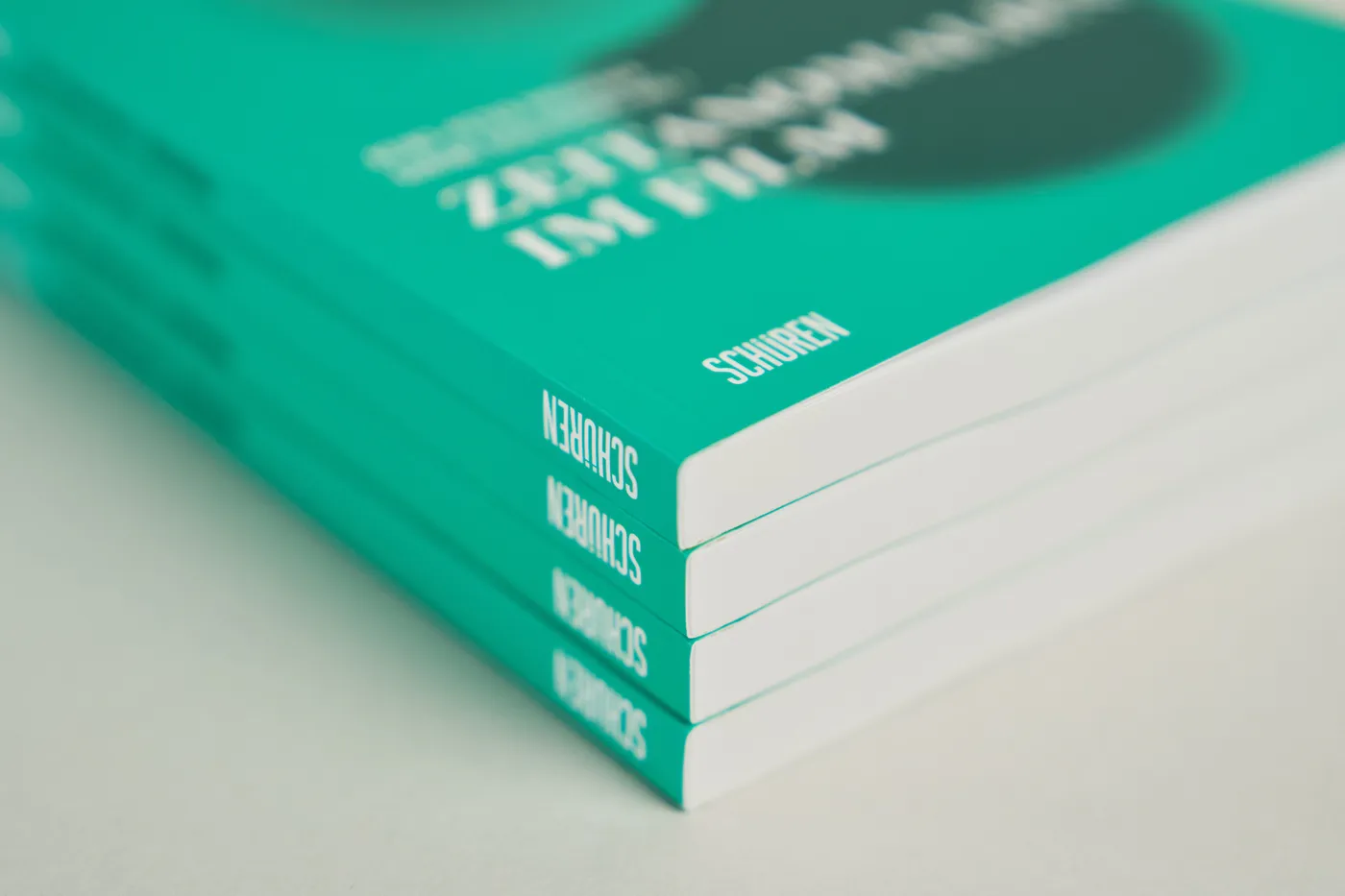 Vier klebegebundene Bücher mit grünem Umschlag liegen gestapelt, auf jedem Rücken steht der Verlagsname.