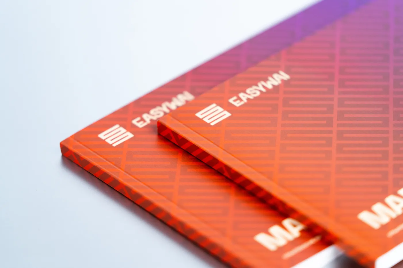 Zwei klebegebundene Broschüren mit orange-violettem Muster-Umschlag liegen versetzt übereinander.