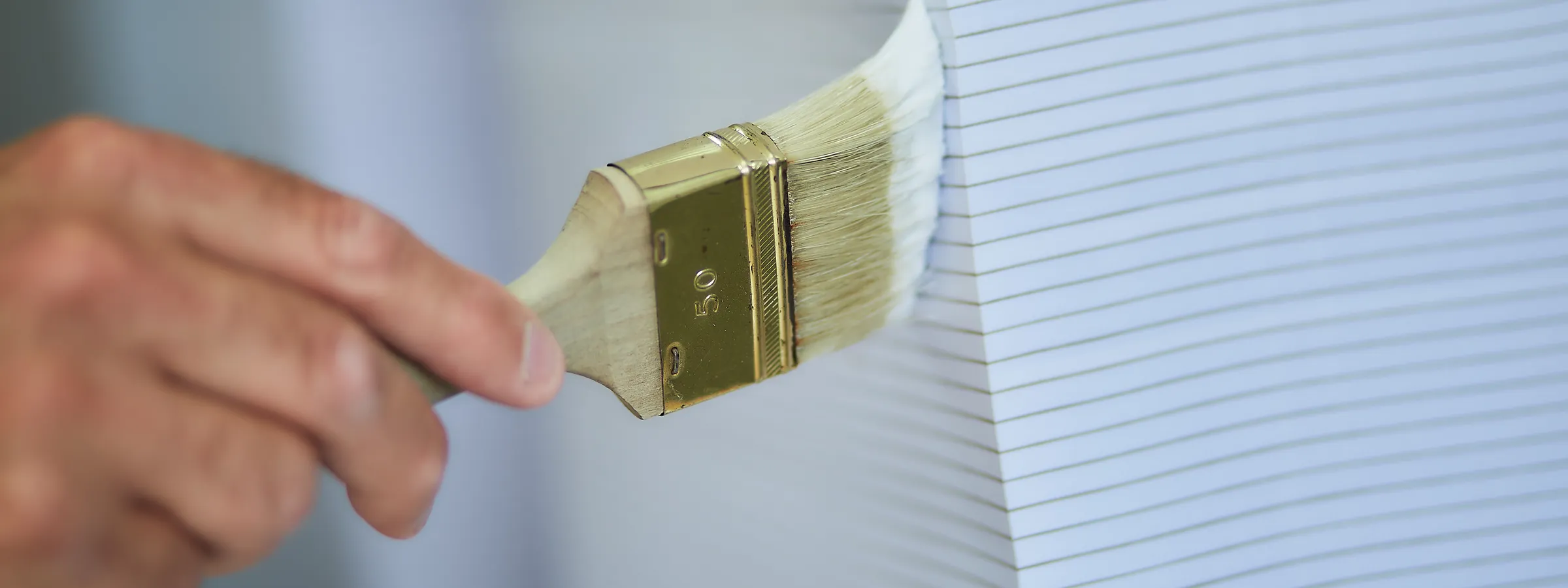Eine Hand streicht mit einem breiten Pinsel weißen Leim auf die Kante eines hohen Papierstapels.