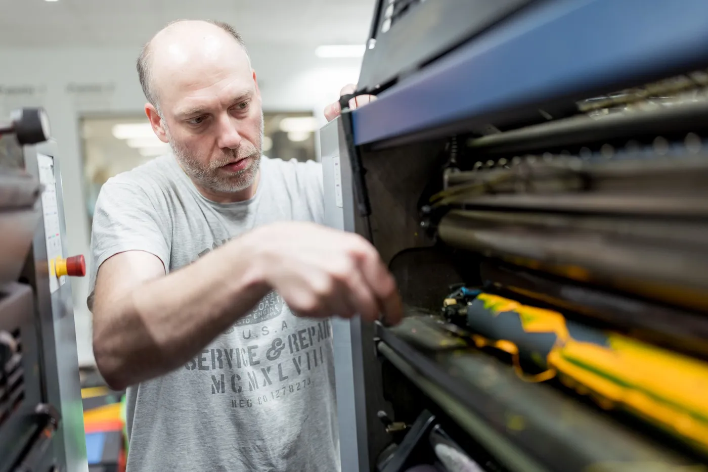 Ein Drucker greift in das geöffnete Farbwerk der Offsetmaschine.