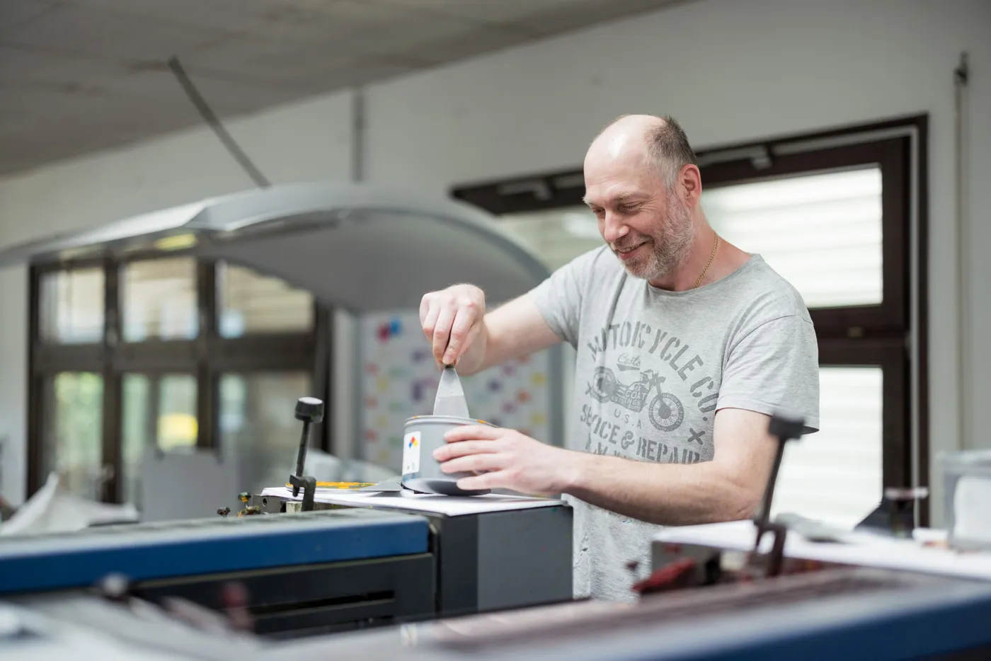 Ein Drucker nimmt an der Offsetmaschine mit dem Spachtel Farbe aus einer Dose.