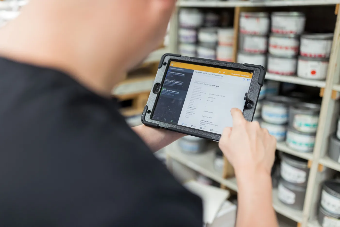 Ein Drucker tippt vor einem Regal voller Farbdosen auf ein Tablet.