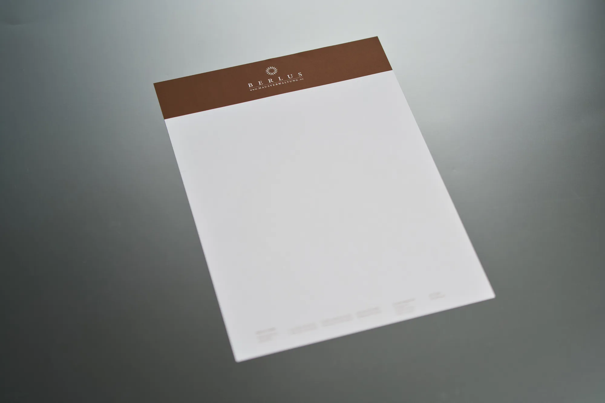 Weißer Briefbogen mit braunem Kopfbalken in Sonderfarbe auf grauem Grund.