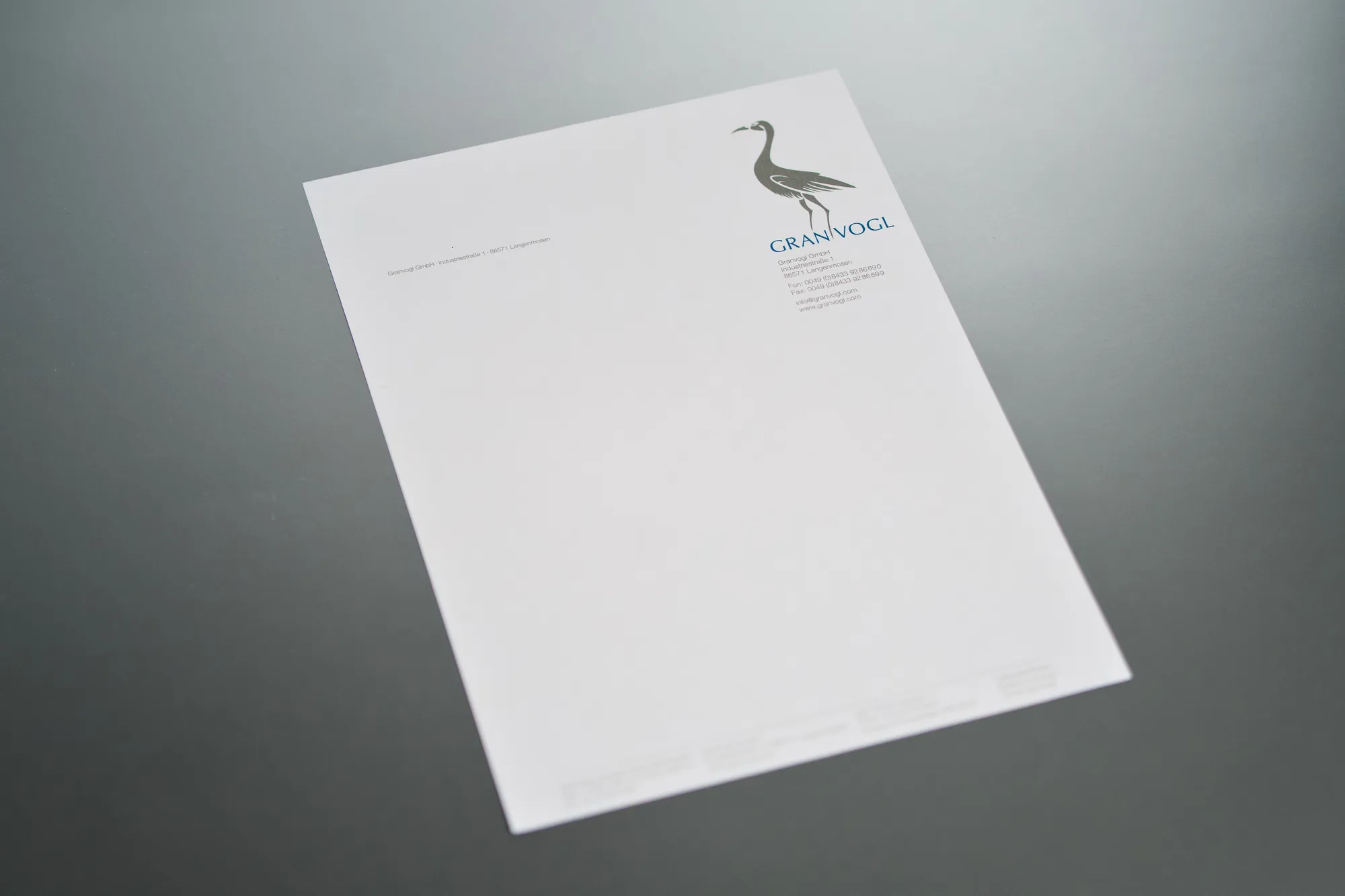 Weißer Briefbogen mit einem Kranich-Logo in zwei Sonderfarben auf grauem Grund.