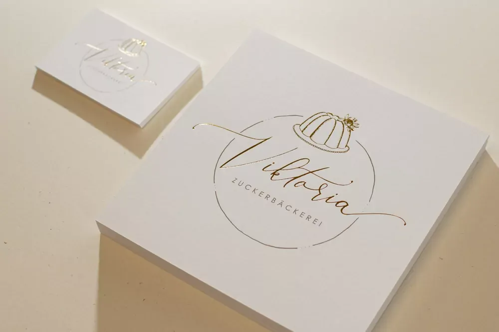 Weiße Karte mit goldener Heißfolienprägung „Viktoria Zuckerbäckerei“ und einer Gugelhupf-Zeichnung.