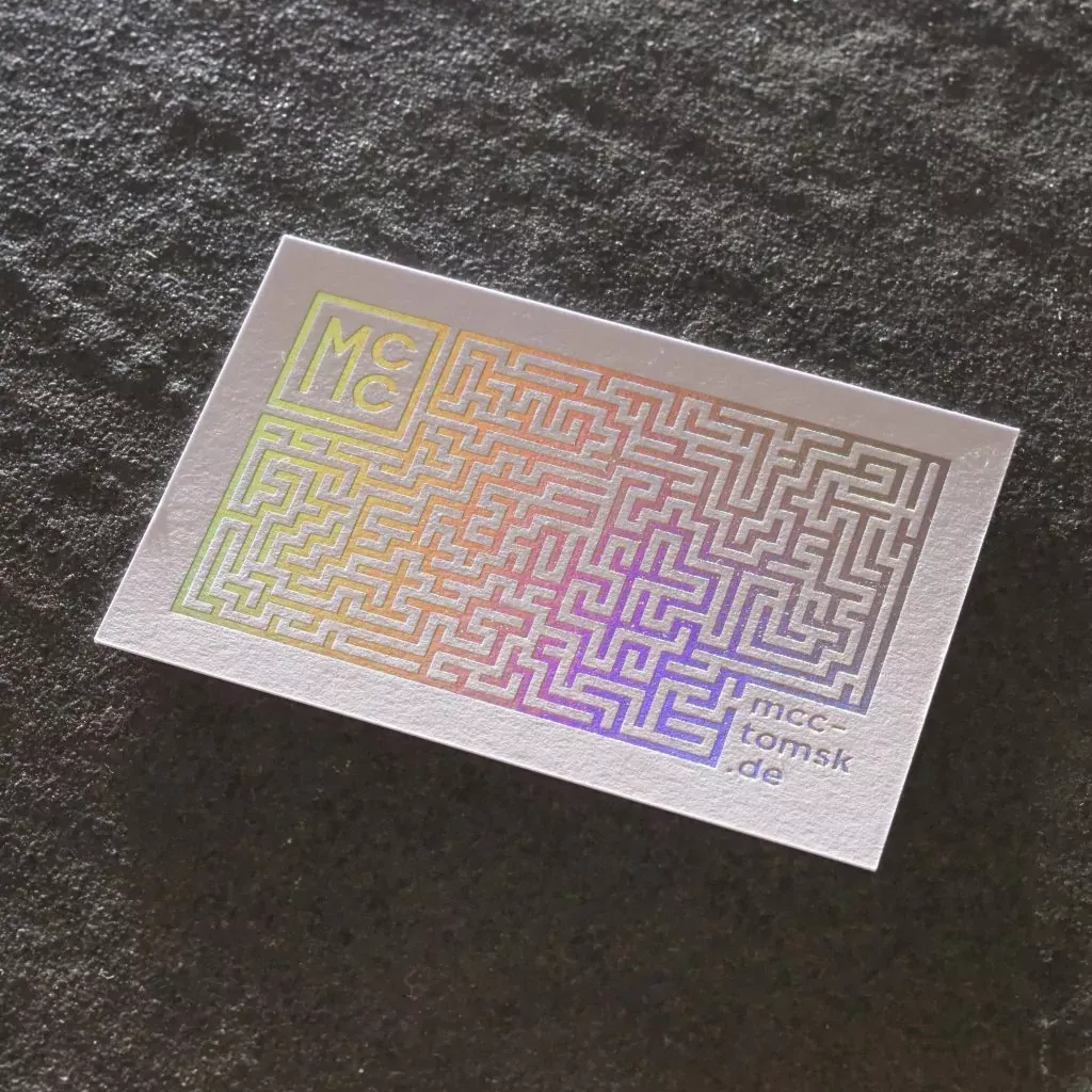 Weiße Visitenkarte mit einem Labyrinth in holografisch schimmernder Laserfolie auf dunklem Stein.