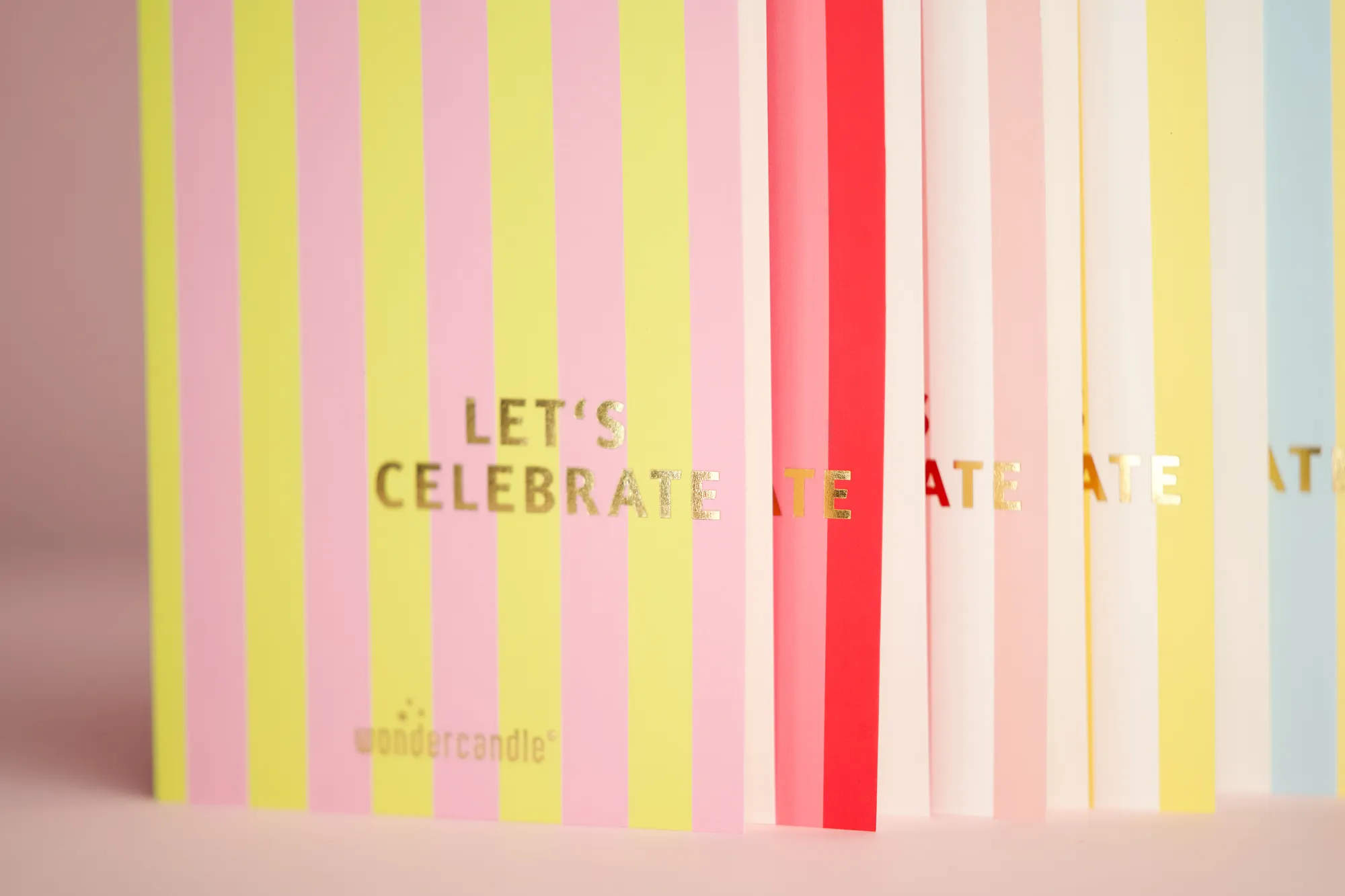 Aufgestellte Klappkarten mit farbigen Streifen und goldenem Schriftzug „Let’s celebrate“.