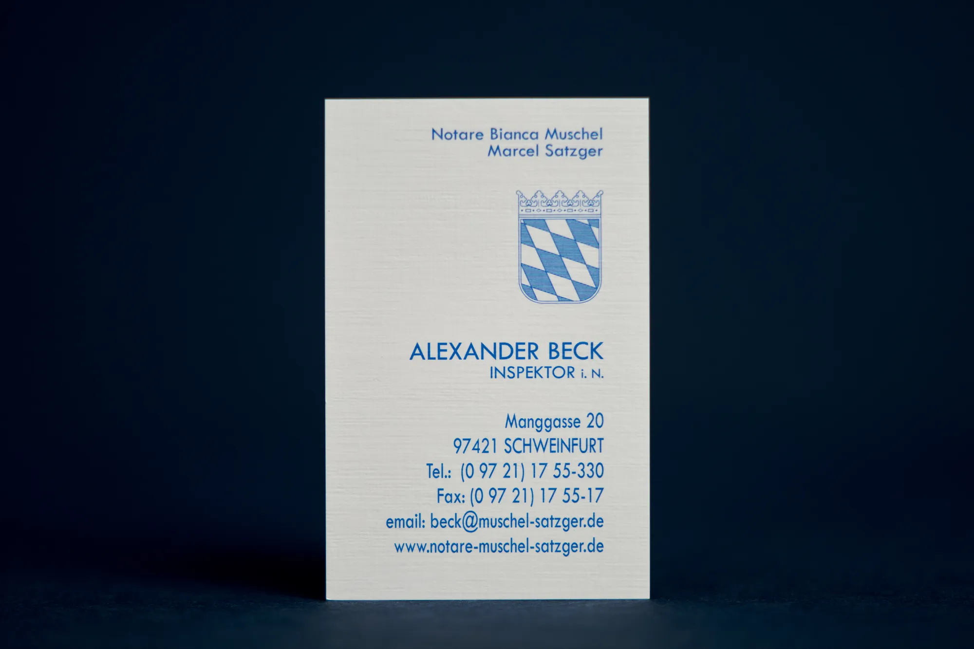 Visitenkarte eines Notariats mit bayerischem Wappen und blauer Schrift auf Leinenpapier.