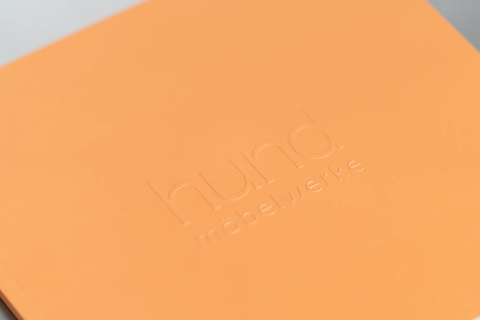 Orangefarbener Broschürenumschlag mit hochgeprägtem Schriftzug im Streiflicht.