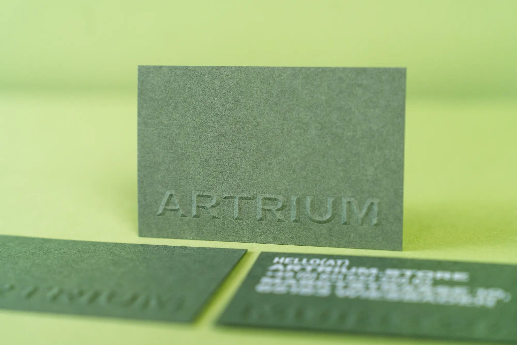 Dunkelgrüne Visitenkarten mit hochgeprägtem Logo „Artrium“ und Weißdruck.