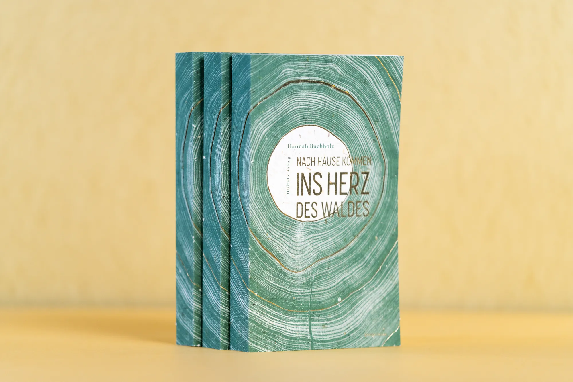 Taschenbücher „Ins Herz des Waldes“ mit grünem Jahresring-Motiv auf gelbem Grund.