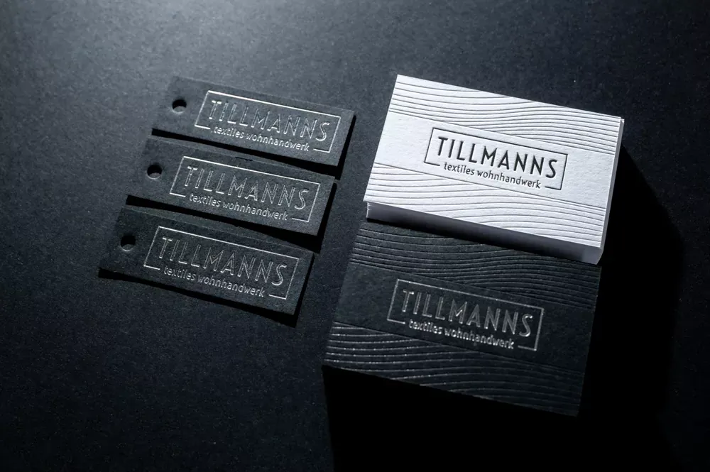Visitenkarten auf Colorplan White Frost und Ebony mit silberner Heißfolie, daneben gebohrte schwarze Anhänger.