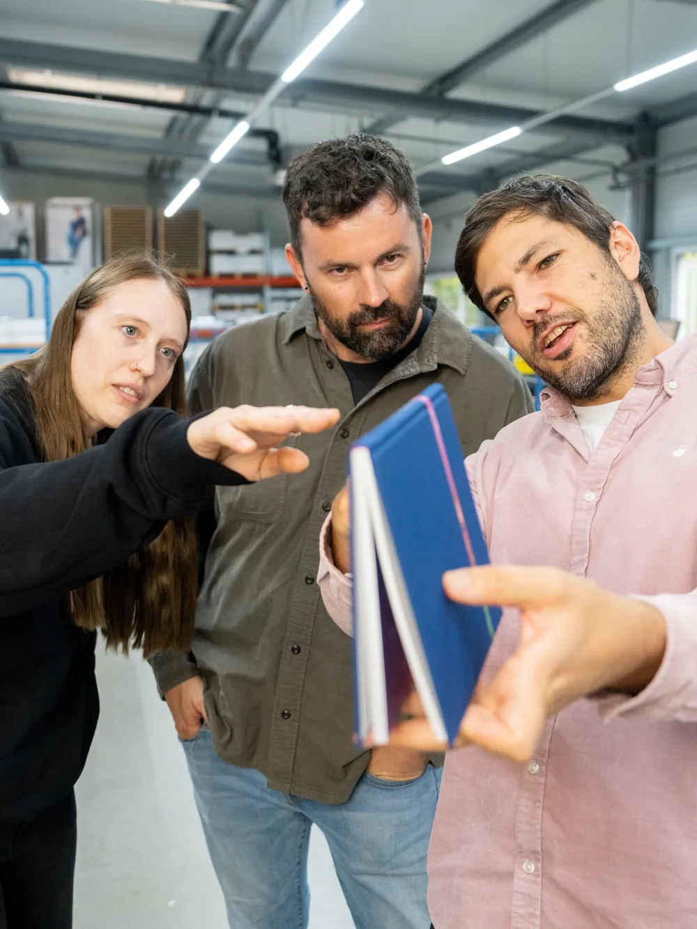Drei Kollegen beugen sich über ein blau eingebundenes Buchmuster und besprechen den Einband.