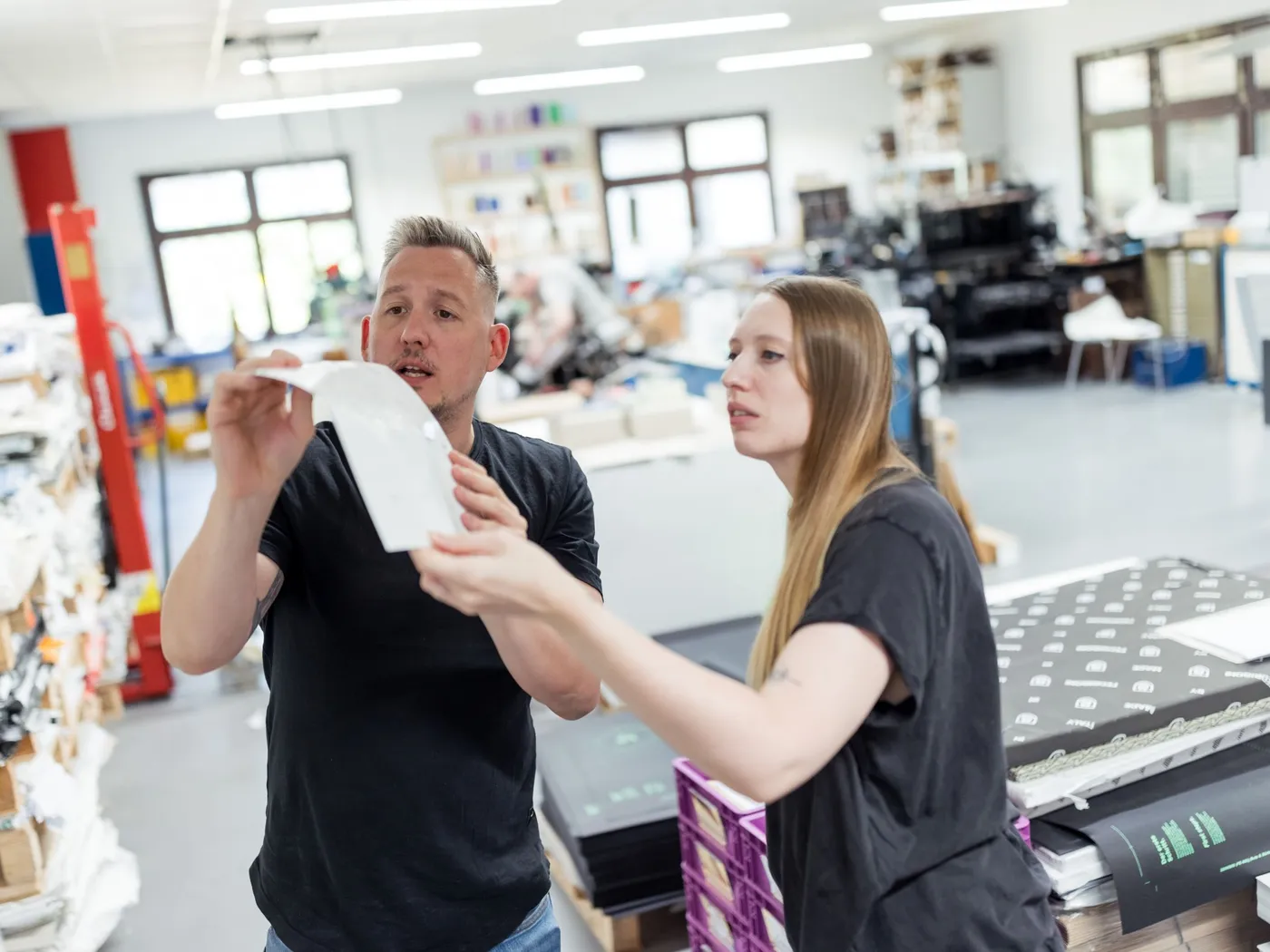 In der Werkstatt in Karlsruhe prüfen ein Kollege und eine Kollegin einen gestanzten Papierbogen.
